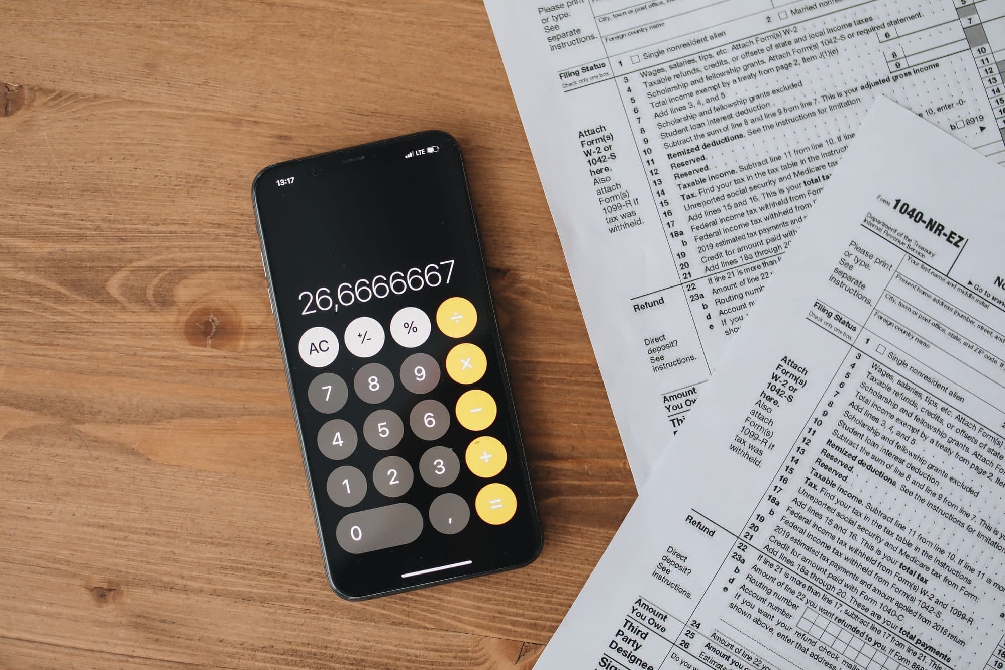 Tax forms beside a smartphone calculator on a wooden desk